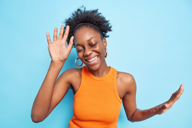 Free photo beautiful carefree dark skinned woman dances with arms raised to party music closes eyes from pleasure enjoys life