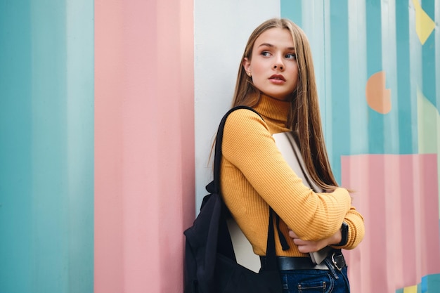 Free photo beautiful casual student girl with laptop thoughtfully looking away over colorful background outdoor