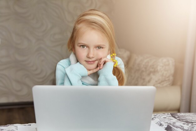開いているラップトップコンピューターの前に座っている美しい白人金髪少女