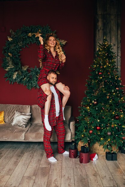 Beautiful caucasian couple in love in the same sleepwear decorates christmas tree together at home