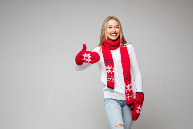 Beautiful caucasian female in white sweater, red scarf and red mittens likes something, picture isolated on white background