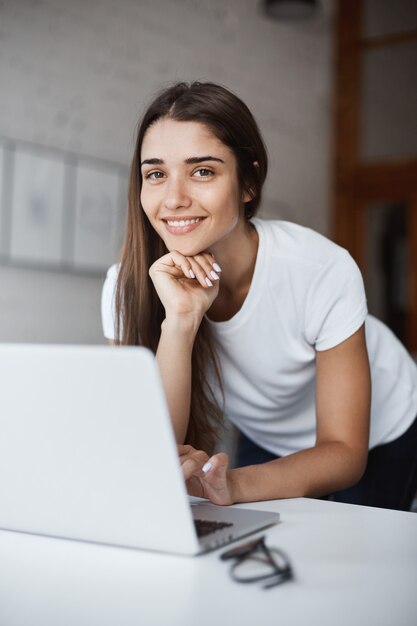 Beautiful caucasian girl using laptop computer watching cat videos on internet looking at camera smiling.