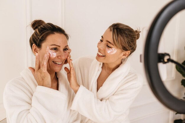 Beautiful caucasian girls in bathrobes struggle with bruises and dark circles under eyes with patches. Skin care and health concept