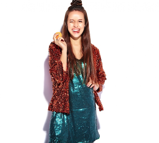 Beautiful caucasian smiling hipster brunette woman model in bright shinny reflecting summer stylish jacket and green dress isolated . Eating french macaroon and showing her tongue