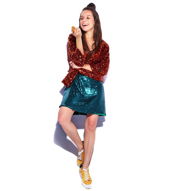 Beautiful caucasian smiling hipster brunette woman model in bright shinny reflecting summer stylish jacket and green dress isolated . Eating french macaroon