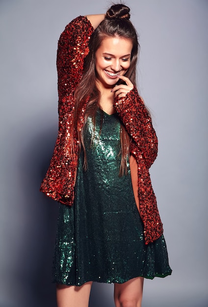Бесплатное фото Красивая кавказская усмехаясь модель женщины брюнет битника в яркой shinny отражая стильную куртку лета и зеленое платье представляя на сером цвете
