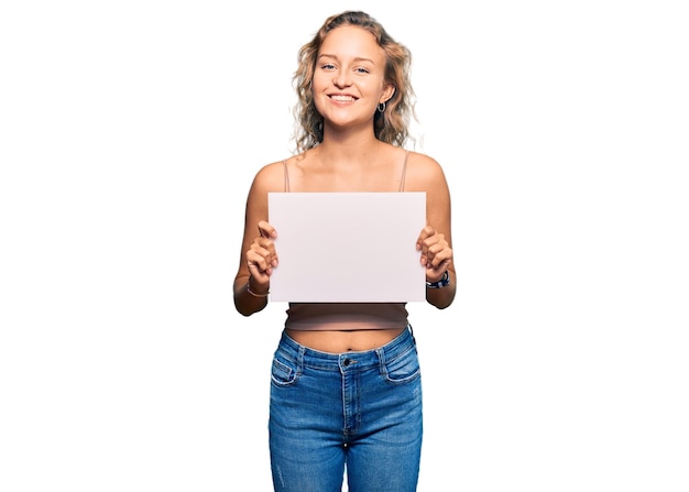 Free photo beautiful caucasian woman holding blank empty banner looking positive and happy standing and smiling with a confident smile showing teeth