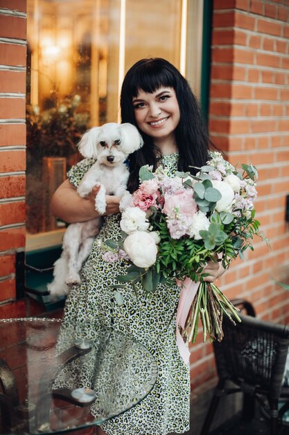 Beautiful caucasian woman holding her white dog and flowers