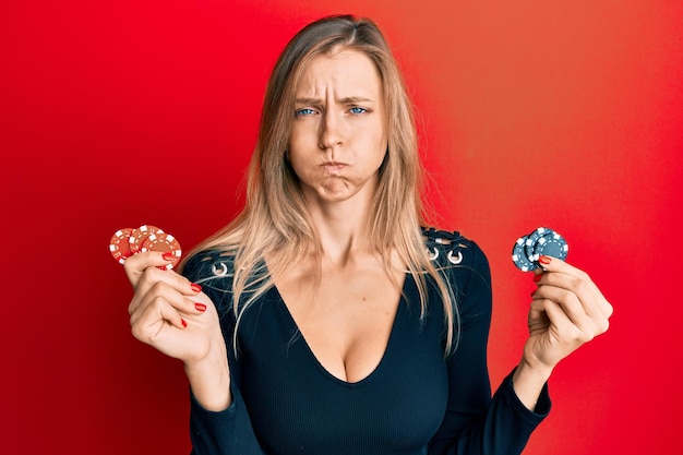 Beautiful caucasian woman playing poker holding casino chips puffing cheeks with funny face mouth inflated with air catching air