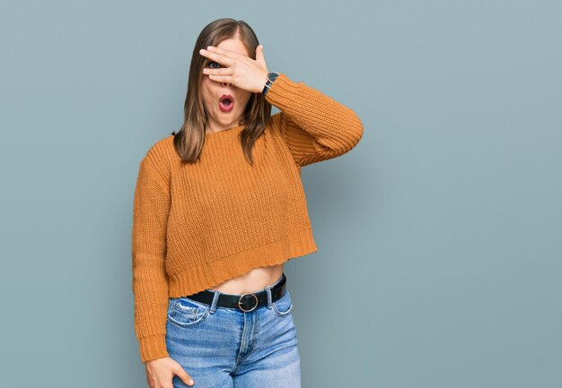 Beautiful caucasian woman wearing casual clothes peeking in shock covering face and eyes with hand, looking through fingers with embarrassed expression.