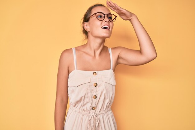 Beautiful caucasian woman wearing summer dress very happy and smiling looking far away with hand over head searching concept