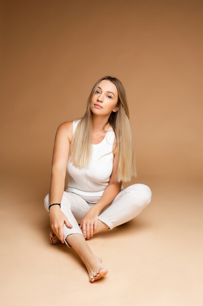 Beautiful caucasian woman with fair hair sits on the floor, picture isolated on brown background
