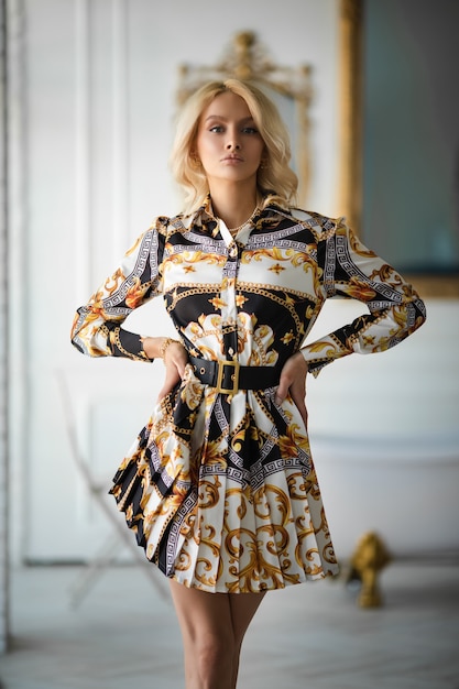 Beautiful caucasian woman with wavy blonde hair in new stylish dress poses for the fashion magazine in luxurious apartments