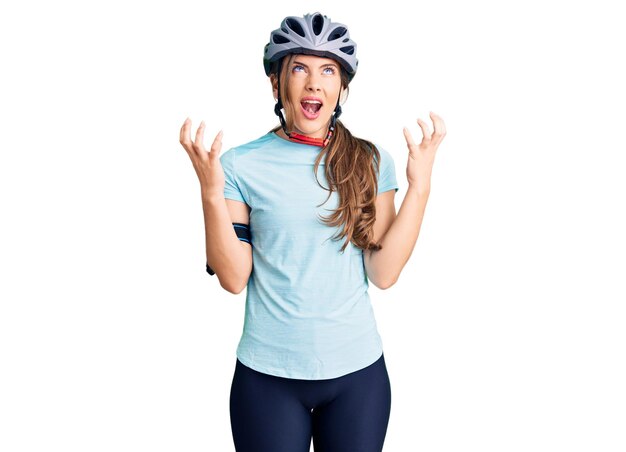 Beautiful caucasian young woman wearing bike helmet crazy and mad shouting and yelling with aggressive expression and arms raised. frustration concept.