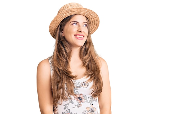 Beautiful caucasian young woman wearing summer hat looking away to side with smile on face, natural expression. laughing confident.