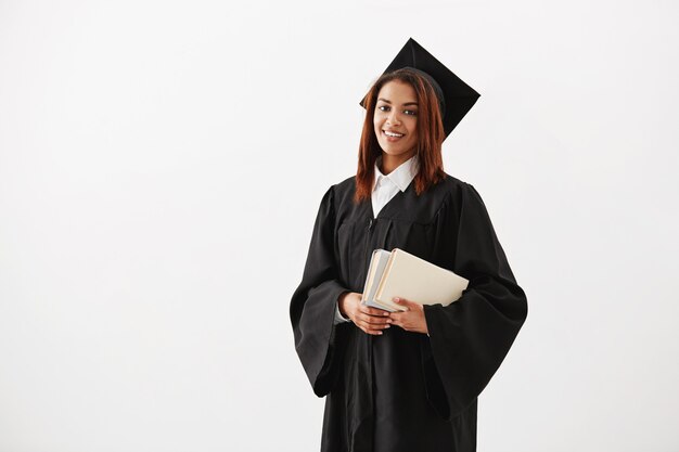 Beautiful cheerful african female graduate smiling holding books. Copy space.