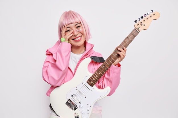 Foto gratuita la bella musicista femminile allegra suona la chitarra elettrica essendo membro del popolare gruppo rock ha l'acconciatura rosa indossa una giacca