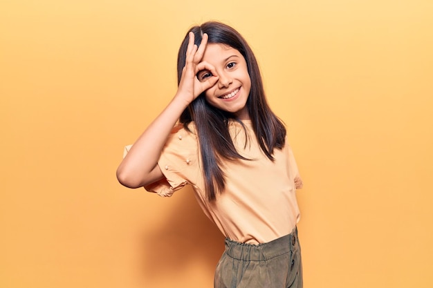 Beautiful child girl wearing casual clothes smiling happy doing ok sign with hand on eye looking through fingers