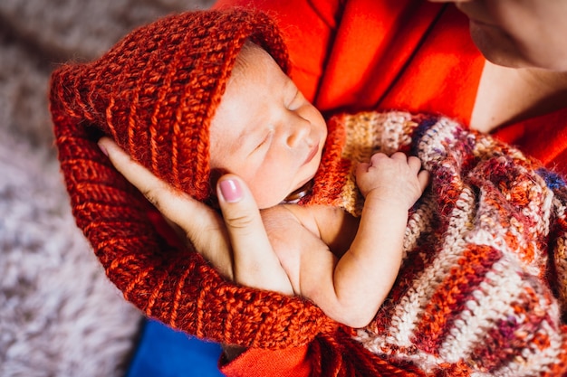 Beautiful child in red hat sleeps in mother's tender arms 