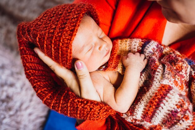 Красивый ребенок в красной шляпе спит в нежных руках матери