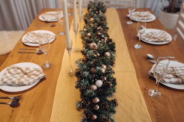 Free photo beautiful christmas serving table with candles and fir-tree decoration at cozy modern interior close-up. celebrating december holiday new year surrounded by seasonal decorated glasses and plates