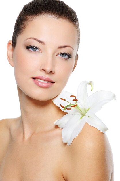 Beautiful clear female face with health skin and white lily on her shoulder