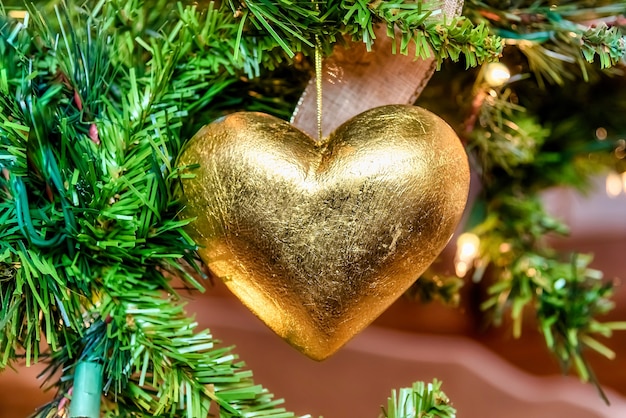 Beautiful closeup of a golden heart-shaped ornament on a Christmas tree with lights