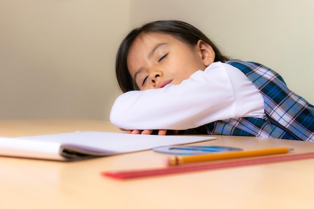 Beautiful Colombian girl wearing a school uniform sleeping on the desk while doing homework