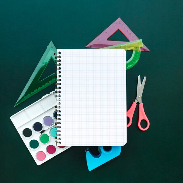 beautiful composition with notebook scissors, ruler and watercolors on green wood background