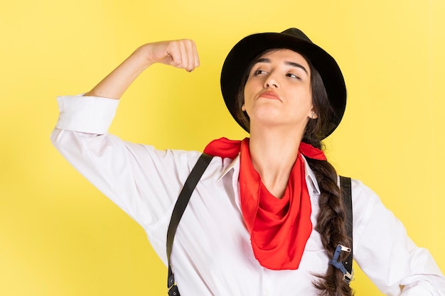 Free photo beautiful confident cowgirl squeezed her bicep and standing on yellow background high quality photo