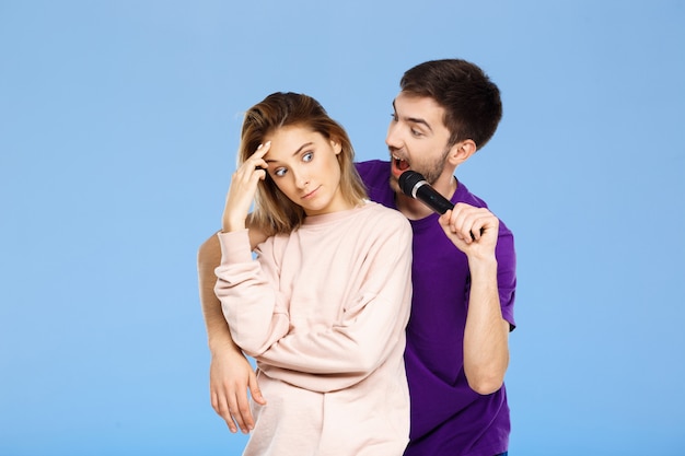 Beautiful couple over blue wall. Man singing in microphone girl didpleased.