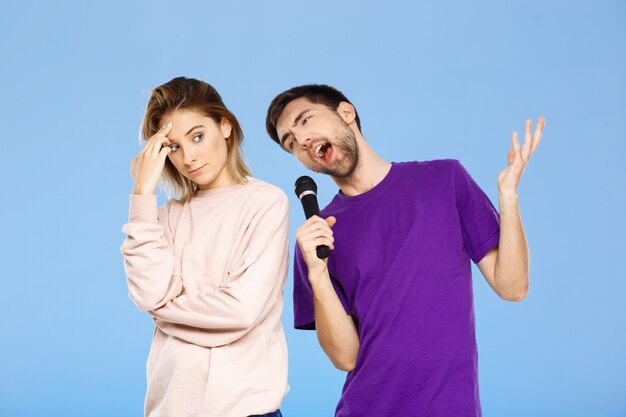 Beautiful couple over blue wall man singing in microphone girl displeased.