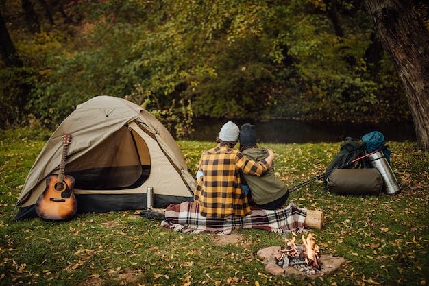 Beautiful couple enjoying nature near tent sitting on log