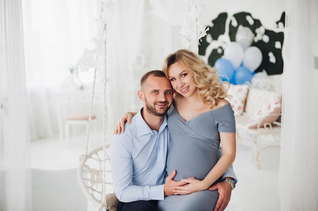 Beautiful couple handsome man and pregnant woman in long gray dress holding smart phone and taking self portrait Romantic family mom and dad expaacting child macking photo together