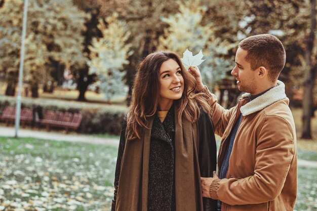 Beautiful couple is enjoying day walk at autumn park, man is holding maple leaf.