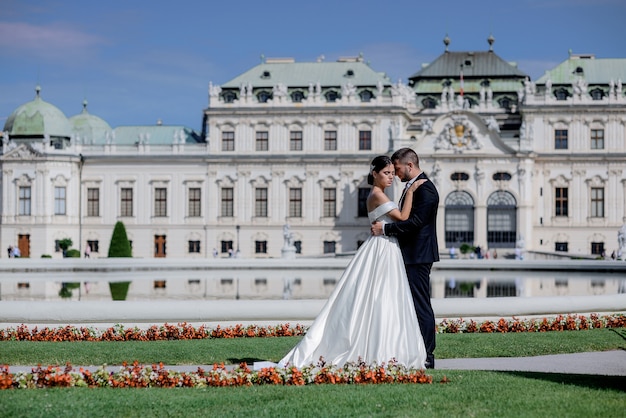Красивая влюбленная пара в свадебных нарядах перед дворцом в прекрасный солнечный день, свадебное путешествие