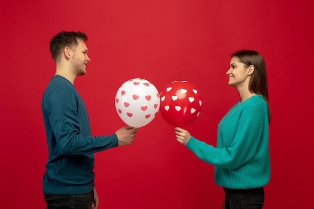 Beautiful couple in love with balloons on red studio wall