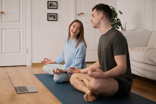 Бесплатное фото Красивая пара вместе занимается йогой дома, используя ноутбук, принимая онлайн-классы йоги