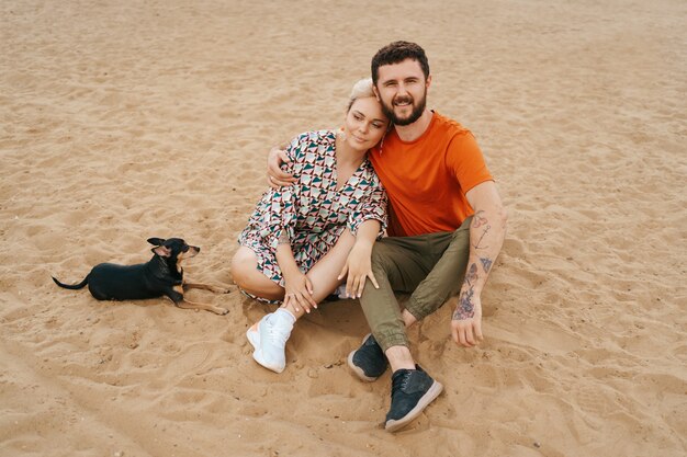 Beautiful couple relaxing on sand hugging and kissing while playing with their positive dog