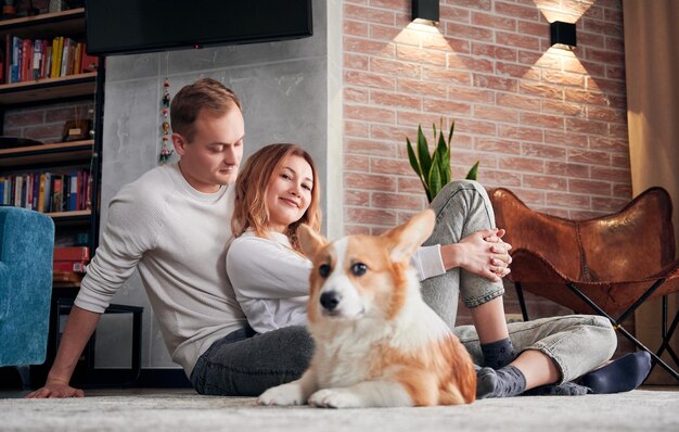 Beautiful couple sitting on the floor with adorable Corgi