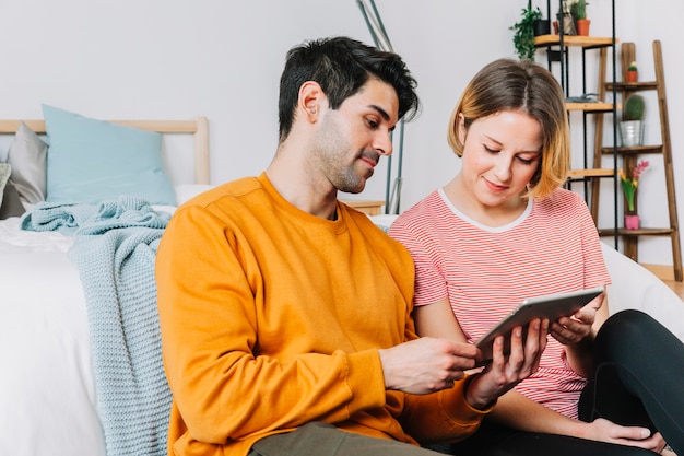 Foto gratuita belle coppie facendo uso della compressa vicino al letto