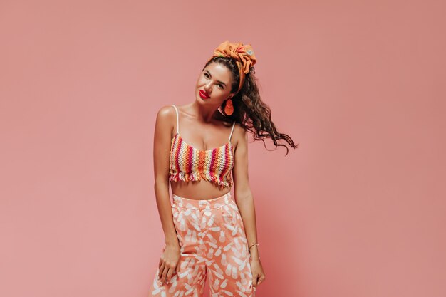 Beautiful curly haired woman with stylish accessories in fashionable bright clothes playing her hair and looking at front