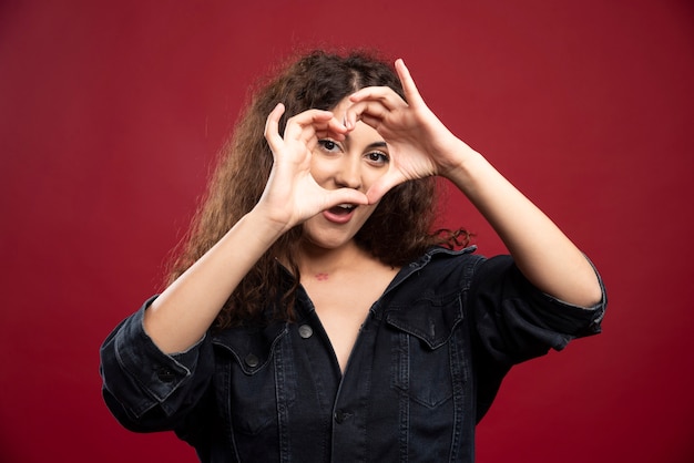 Free photo beautiful curly woman giving heart gesture.