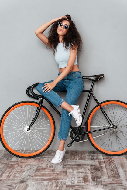 Beautiful curly woman in sunglasses posing with bicycle