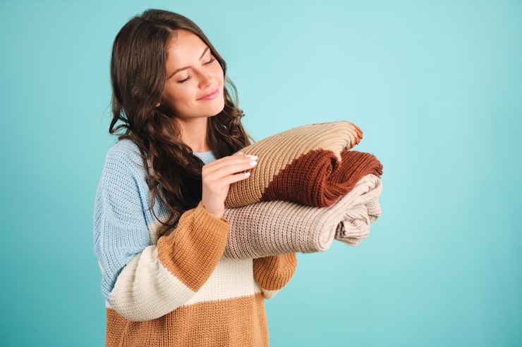 Free Photo beautiful cute girl dreamily holding cozy knitted sweaters in hands over blue background