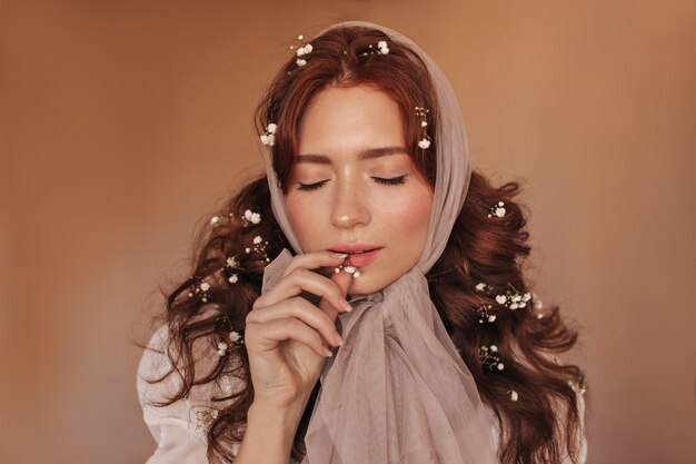 Beautiful dark-haired woman biting white flower. Woman in headscarf posing on isolated background.