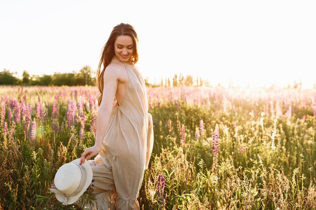 Beautiful dark-haired woman in a summer dress in a field of blooming lupine flowers 