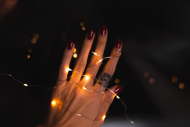 Красивая темная фотография женских пальцев рук с большим серебряным кольцом из цветов и светящихся огней