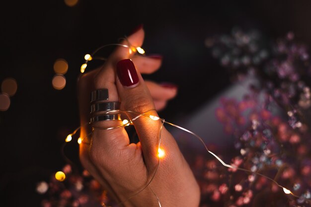 Beautiful dark photo of womans hand fingers with big silver ring on of flowers and glowing lights