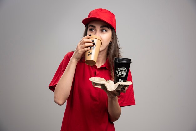 Beautiful delivery woman in red uniform drinking coffee. 